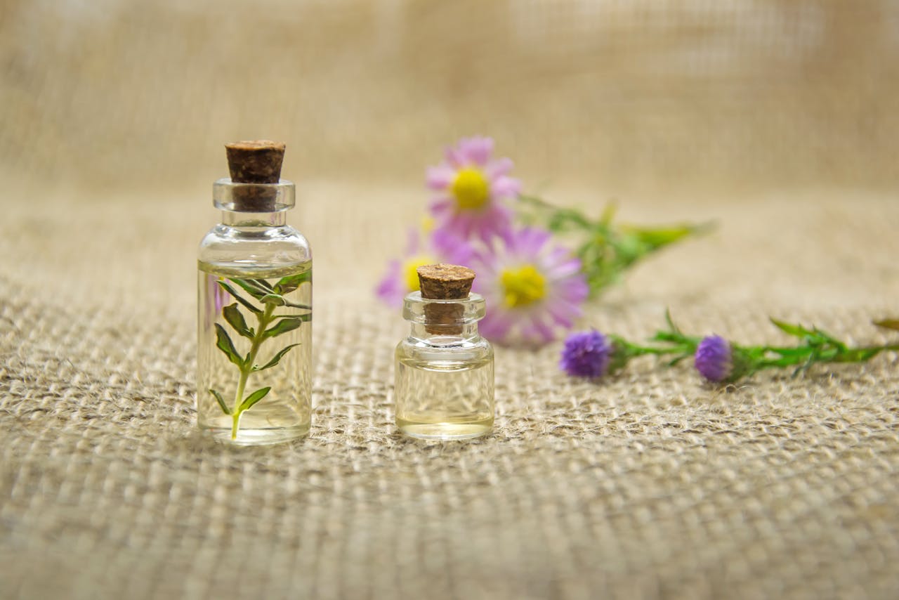 about-us Glass bottles with essential oils and fresh flowers on burlap fabric creating a natural aroma.
